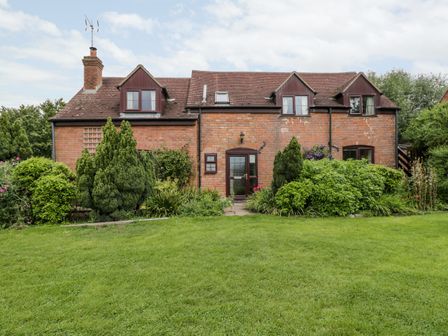 A brick house with a tiled roof surrounded by green shrubs and a lawn at Lawn Farm Cottage in Churcham near Gloucester