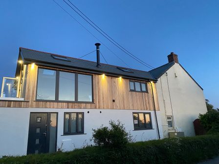 A two-story house with wood paneling and multiple windows and a black door at Pen Chy in Porthleven