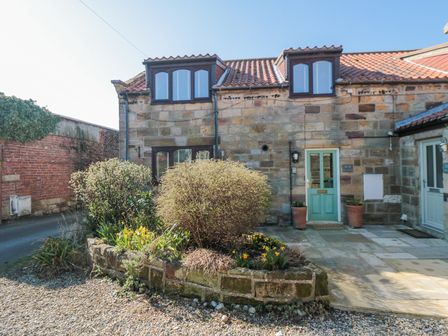 A stone cottage with a green door and garden bed in front at Barn Cottage in Hinderwell