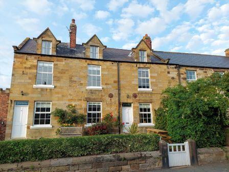 A stone terraced house with white doors and windows a bench and garden furniture in front of it at Fair Holme in Hinderwell