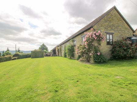 A stone building with windows surrounded by grass and flowering plants at The Onibury in Craven Arms