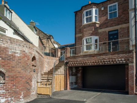 A brick house with a black garage door a staircase with a wooden gate and a glass railing at Salt Bay Whitby