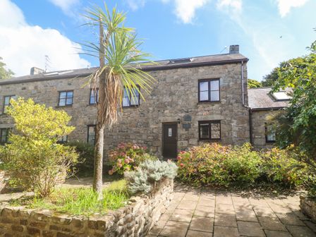 Front view of a stone cottage with multiple windows a central door and surrounding garden at Barn Cottage in Gulval near Penzance