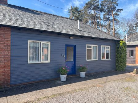 A blue wooden house exterior with three windows and a blue door with potted plants on the ground at Stable Cottage in Triscombe