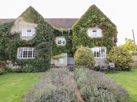 A house covered in ivy with shrubs and a grassy garden at The Malins in Blockley