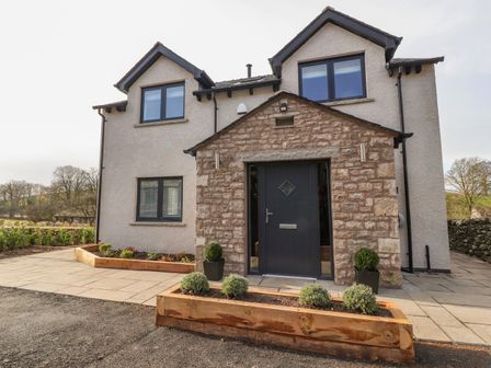 The front exterior of a two-story house with a stone entryway and a dark front door at Laundry Cottage in Leasgill near Milnthorpe