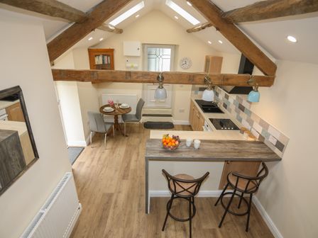 A kitchen and dining area with wooden beams overhead a wooden breakfast bar with stools and a small round dining table with chairs at Glan Meon Cottage in Barmouth