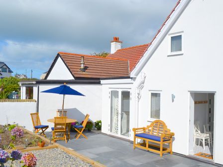 A white house with a patio featuring wooden chairs and a table with a blue umbrella at One Dolfor in Aberdaron