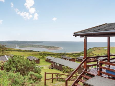 A coastal view with cabins and grassy hills and a covered wooden deck at The Look Out in Aberdovey