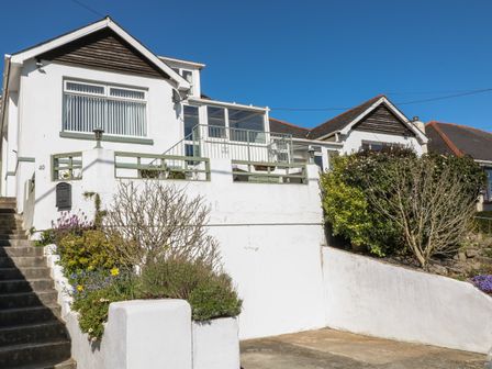 White house with garden bushes and flowers and steps leading to front door at Pebble Lodge in Paignton