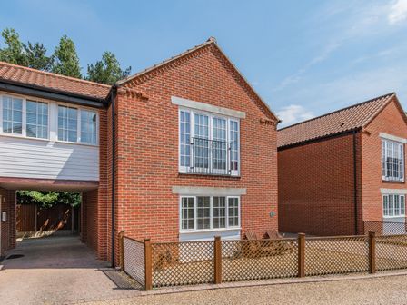 A brick house with white framed windows and a small fenced yard at 26 Burtons Mill in Stalham