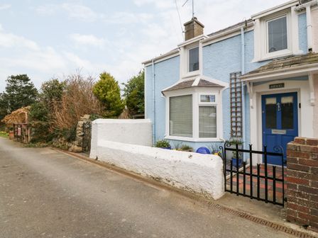 The exterior of a blue house with a blue door behind a black gate and a white wall at Arwel in Nefyn