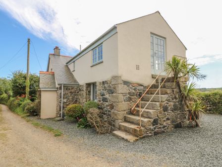 Exterior view of a stone and stucco house with stairs leading to an upper door surrounded by plants at Higher Roskorwell Cottage in St Keverne
