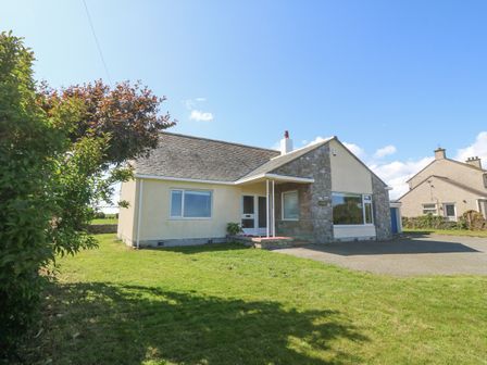 A single-story house with a stone and plaster exterior a driveway and lawn at Glanffraw in Aberffraw Ty Croes