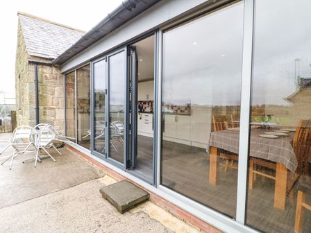 A stone building with folding glass doors leading to a kitchen and dining area at Houghton North Farm Cottage in Heddon-on-the-Wall near Hexham