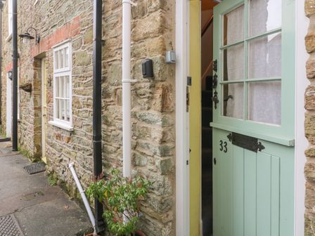 An open green door with the number 33 on a stone building with windows and outdoor pipes at 33 Island Street Salcombe