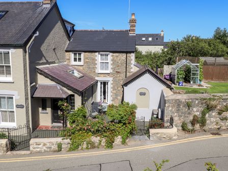A stone house with a small front garden and greenhouse behind a stone wall at Morawel Fach in Newport Pembrokeshire
