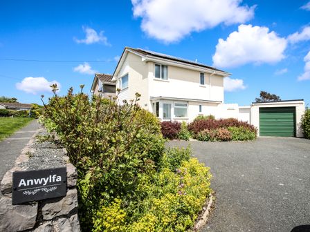 A driveway with plants and bushes leading to a two-story house and garage at Anwylfa in Moelfre