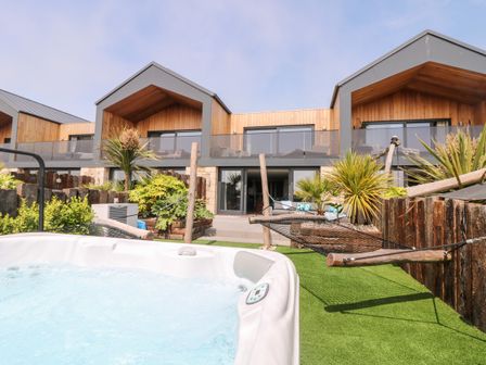 An outdoor area with a hot tub hammock plants and a modern building with balconies at Sennen Skies in Sennen
