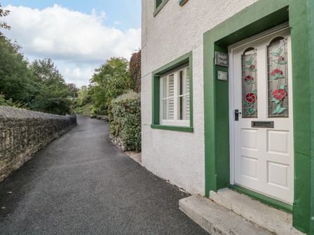A pathway alongside a house with a white door with stained glass and green trim at Endgill Cottage in Ulverston