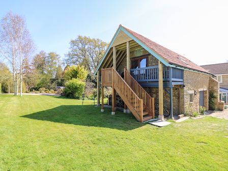 A stone building with wooden stairs leading to a balcony in a garden at Cherrywood Barn in South Petherton
