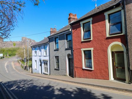 A street with three colored houses and a castle in the background at Ty Coch y Castell in Pembroke