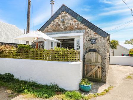 A small stone house with a wooden gate and white wall with umbrella and greenery at Rocket Cart House in Lizard