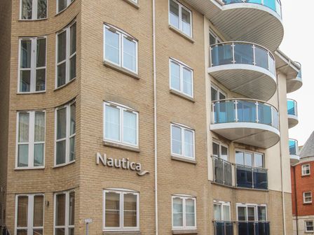Exterior view of a multi-story building with beige brick walls and blue glass balconies at Nautica in Weymouth