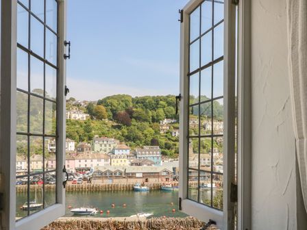A view of a harbor with boats and buildings through open windows at Pixie Cottage in Looe