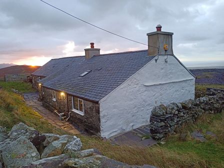 A stone cottage with a slate roof and lit exterior lights in a rural area at Bryn Derwen in Y Fron near Penygroes