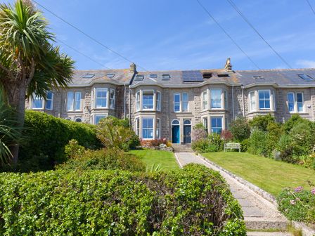 A row of stone houses with green lawns and bushes in front at 6 Albany Terrace in St Ives