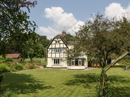 A large garden with grass trees and outdoor furniture outside a white timber framed house at Valley House in Devizes