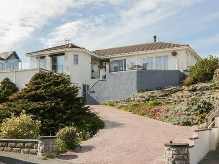 A house with a driveway surrounded by bushes and rocks at Gorwelion in Trearddur Bay