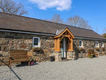 A stone building with small windows wooden benches and a covered entrance at Annex in Nefyn