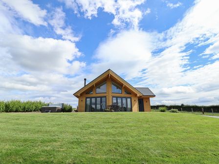 A wooden house with large glass windows a table with chairs and a hot tub on a grassy lawn at Pen Bryn in Cyffylliog near Ruthin