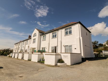 White terraced houses with small concrete patios and private car park under a blue sky at Ketch Cottage in Trearddur Bay