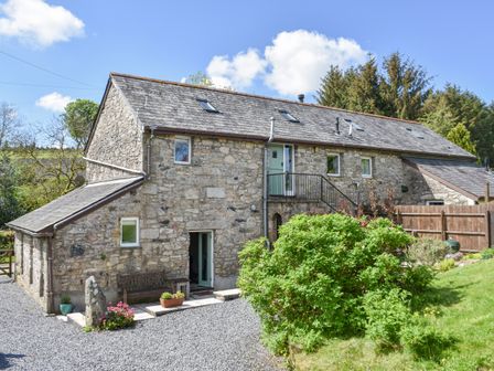 A stone house with a gravel driveway a bench flowers and bushes at Pond Cottage in Lower Cator near Widecombe-In-The-Moor