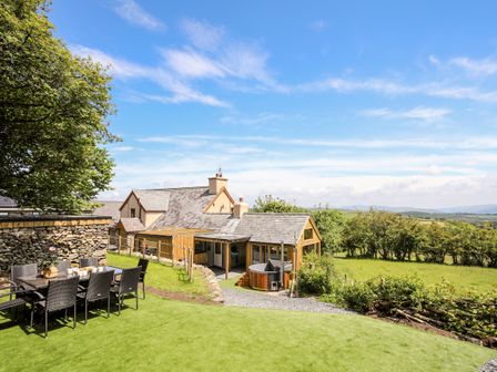 An outdoor dining area with a table and chairs next to a house with a hot tub and green fields in the background at Hafotty Gelynen in Maerdy near Corwen
