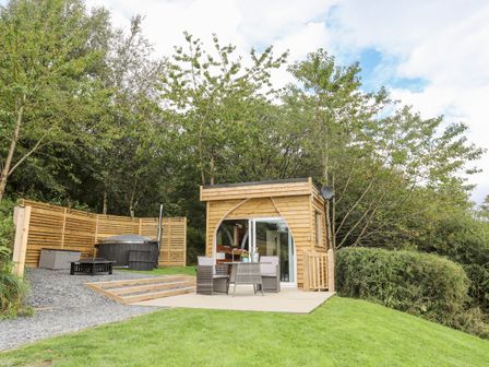 A small wooden cabin with outdoor dining furniture and a hot tub surrounded by trees at Woodland Pod Maerdy near Corwen
