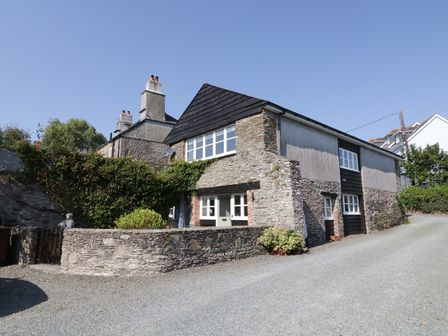 A stone house with white framed windows and a gravel driveway at Crosscombe Barn in Loddiswell