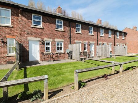 A row of brick terraced houses with patio doors small fenced patios and green lawn at Stephenson Cottage in Whitby