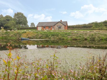 A house with a stone and brick exterior by a pond with a small blue boat and flowers at Hendre in Penybontfawr
