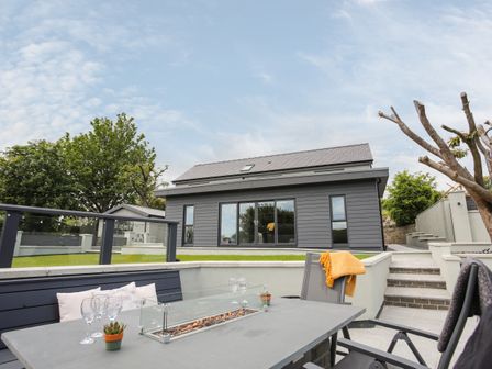 A patio with outdoor furniture and a fire pit with a modern house and garden in the background at Maes Llwyd in Llanbedrgoch near Benllech