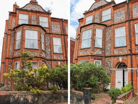 A red brick and stone house with white windows and a white door surrounded by green bushes at Elwin House in Cromer