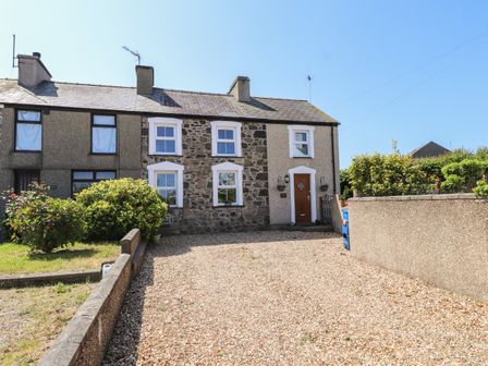 A stone and pebble driveway with bushes and a wooden door on a terraced house at Bwthyn Defaid in Nefyn