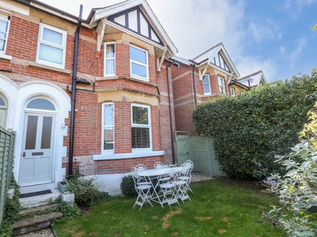 A small garden with a white metal table and chairs outside a brick house with white framed windows at Elm Villa in Wareham