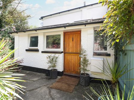 Exterior of a white house with a wooden door flanked by two potted plants and three windows at Mackerel Cottage in Budleigh Salterton