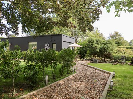 A garden with a gravel path leading to a modern black building and outdoor seating at Kub House in Wigginton Hertfordshire