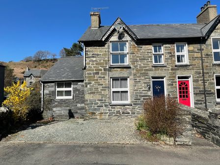 A stone house with blue and red doors and a gravel driveway at 7 Castle Terrace in Dolwyddelan