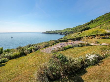 A coastline view with garden and seating area overlooking the sea and hills at 2 Garden Apartment in Hallsands